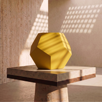 Yellow geometric vase on a stone surface with a textured wall and light filtering through in the background